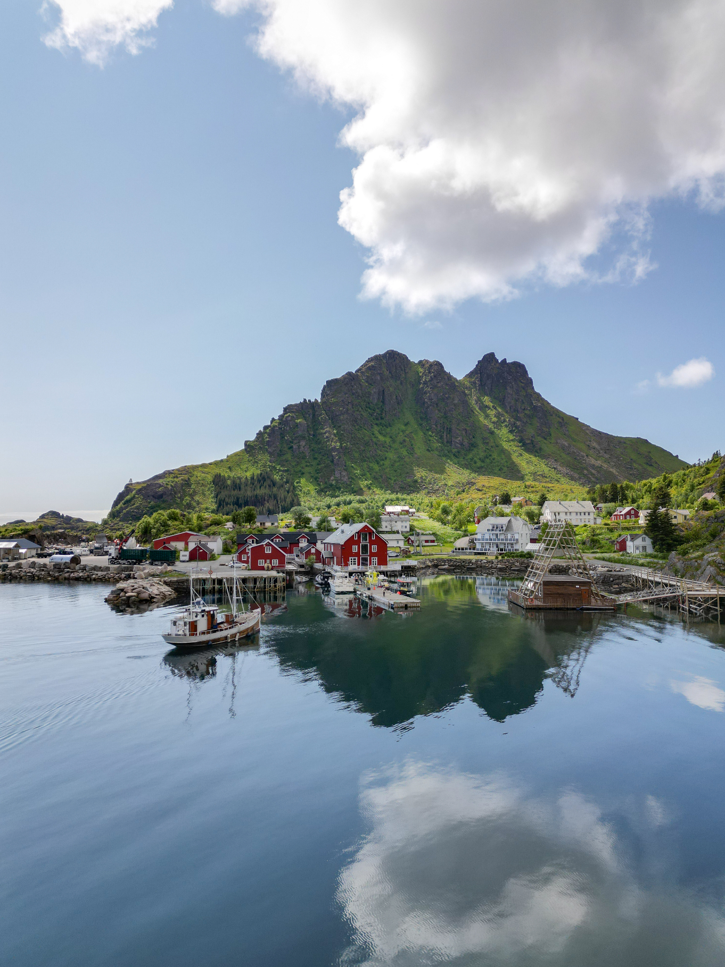 Drone view of the red waterfront houses at Ure beneath a green mountain, mirrored in the fjord